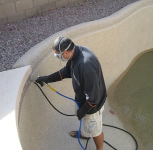 A man in protective gear cleaning a pool with a pressure washer