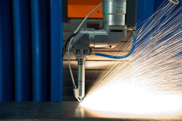 Sparks being produced by a powerful laser cutter on a sheet of metal