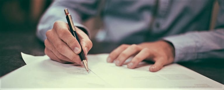 Man writing on a stack of paper with a pen