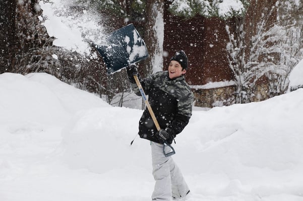 A happy kid throwing snow with a shovel